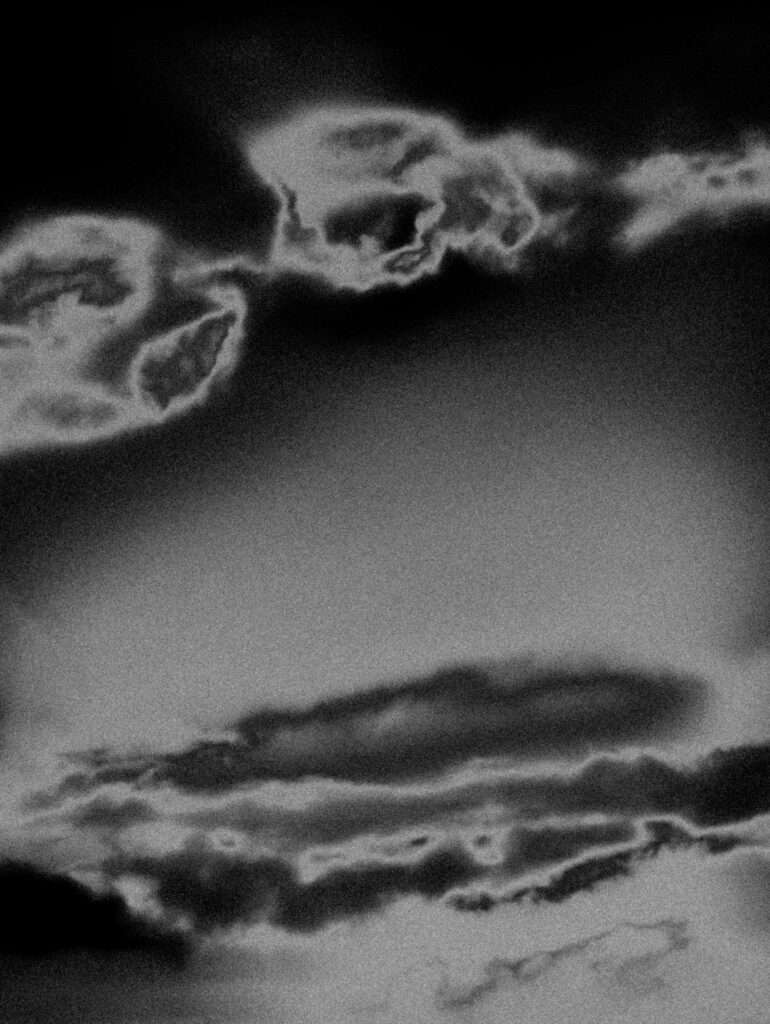Photographie artistique en noir et blanc d’un paysage cotier désert, avec ciel nuageux et plage balayee par le vent. Style granuleux et minimaliste, evoquant la solitude, le silence et la poesie du littoral.