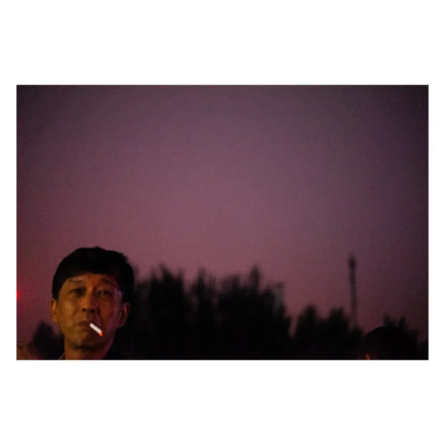 Rencontre humaine insolite dans l'atmosphère crépusculaire de Pékin, mêlant portrait et paysage urbain.