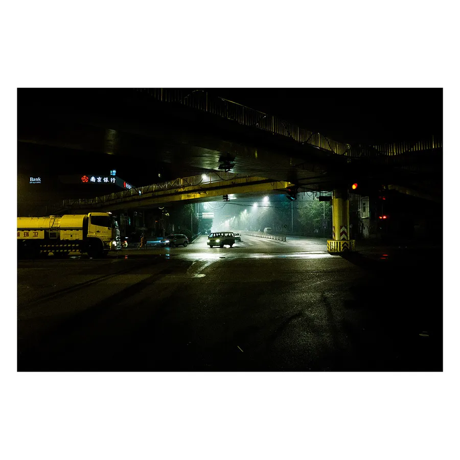 Zone routière pékinoise dans un rendu très contrasté baignée de lumières nocturnes, créant une ambiance urbaine particulière.