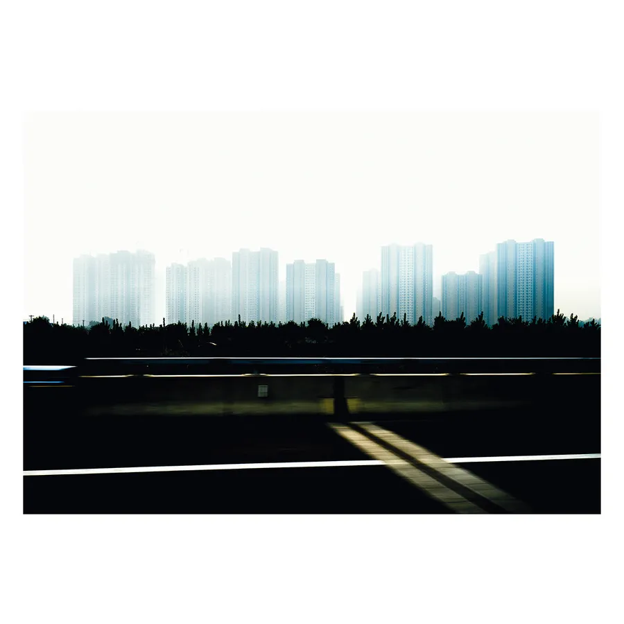 Vue floue du skyline urbain de Pékin depuis une autoroute, capturant l'essence onirique de la ville en mouvement, et de ses zones d’habitation de masses.