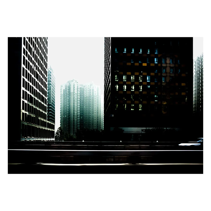 Tour moderne pékinoise saisie dans un flou vertical à bord d'une voiture, évoquant l'ivresse et la vitesse des lumières nocturnes.