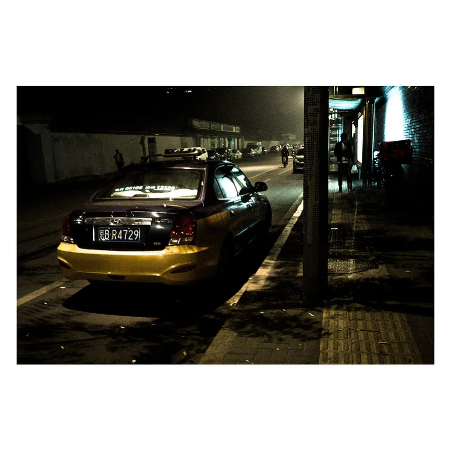 Scène urbaine nocturne avec taxi typique de Pékin, témoignant de l'animation de la ville, lumière contrastée.