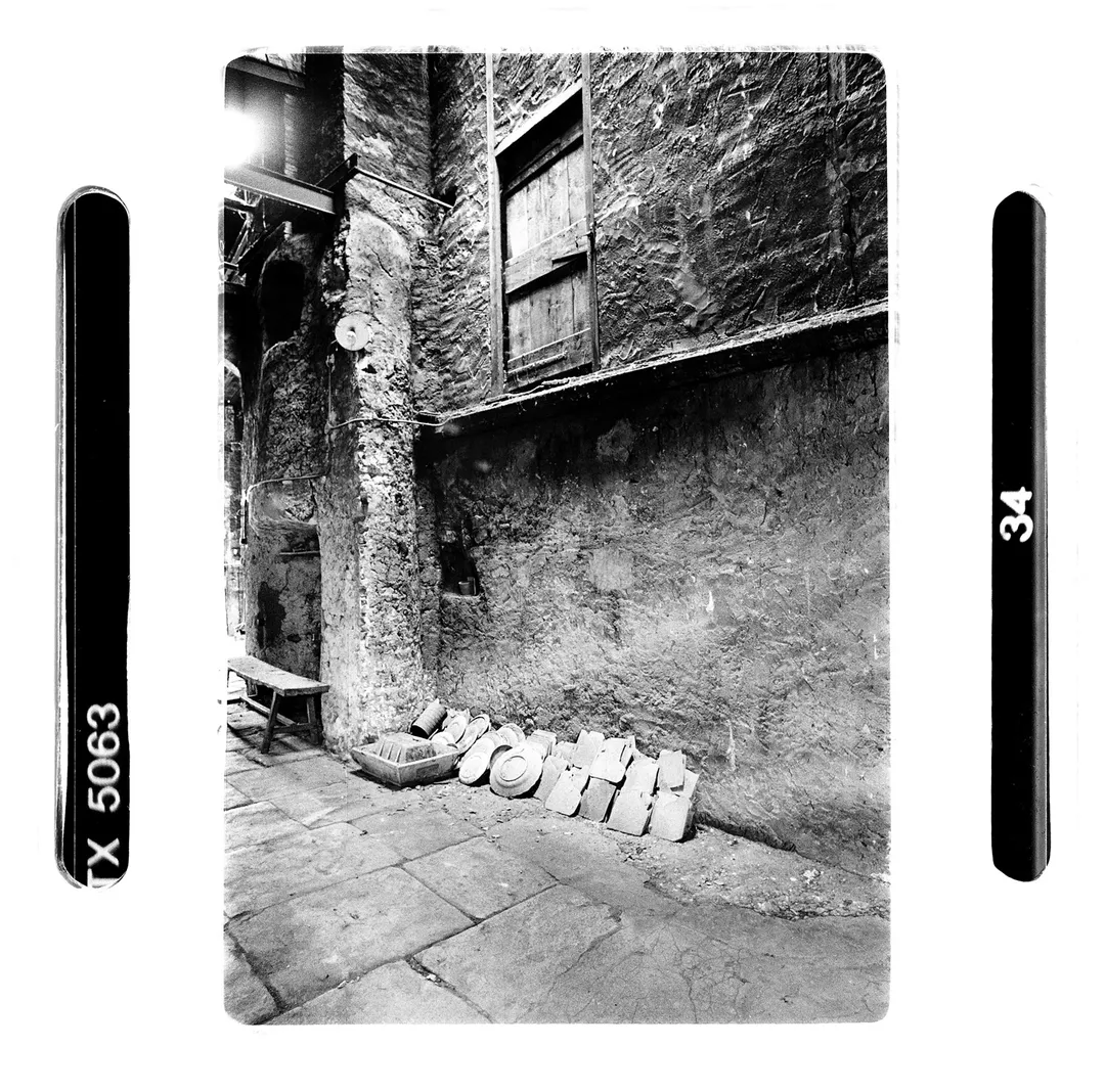 Photo noir et blanc d’une cour d’atelier au poët-laval (Drôme) avec mur ancien, banc et moules de poterie posés au sol, réalisée dans le cadre d’un reportage sur la poterie traditionnelle du village.