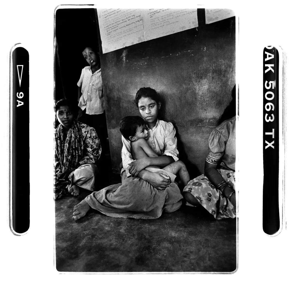Enfant assis triste, tenant un enfant dans ses bras, dans uns salle de classe,en Inde pour photographie humaniste en noir et blanc.