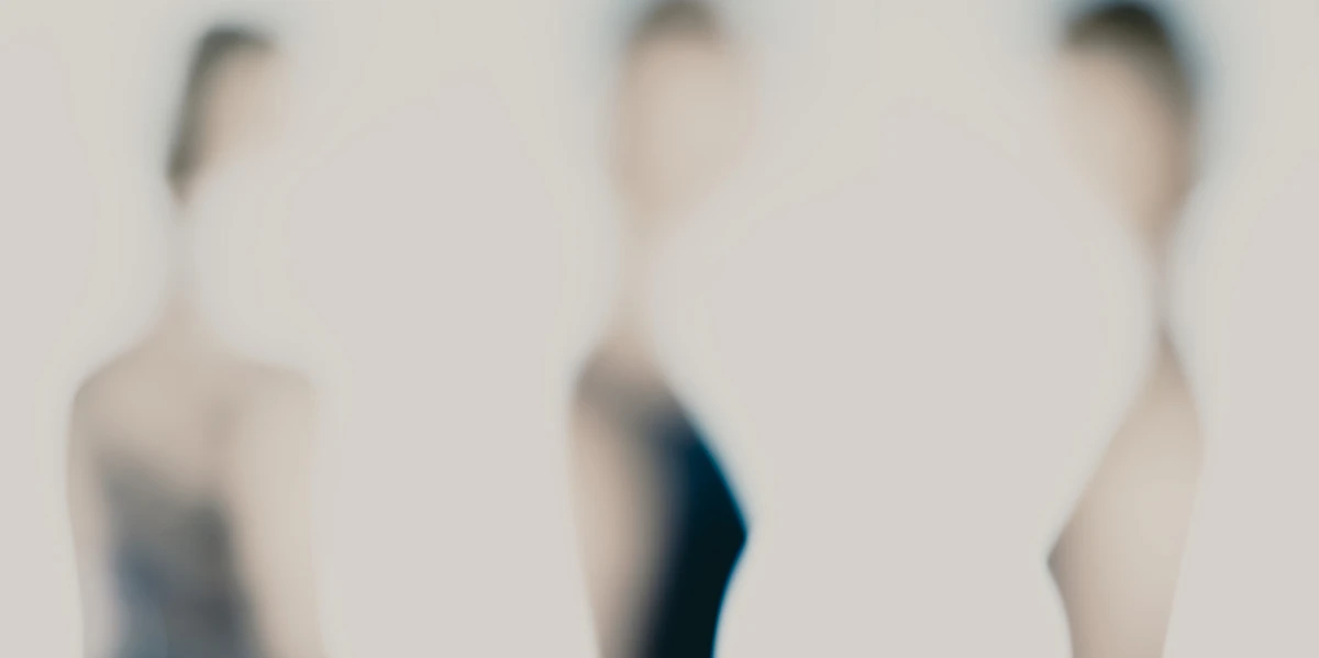Photographie artistique défocalisée : alignement de trois figures humaines très floues sur fond clair, tonalités douces et contours dissous, sensation de triptyque minimal — série « Erasure ».