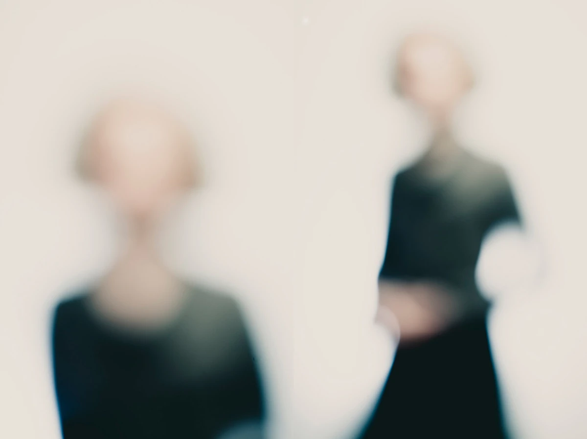 Photographie défocalisée en diptyque : à gauche, buste frontal très flou ; à droite, silhouette entière avec bras croisés, tonalités douces et high-key, identité volontairement estompée — série « Erasure ».
