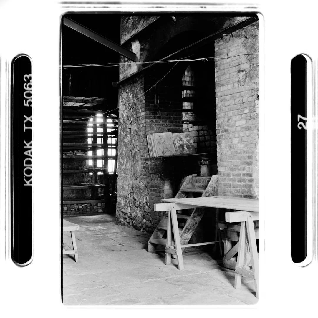 Photo noir et blanc d’un grand four en briques dans un atelier de poterie au poët-laval (Drôme), avec établis en bois et rayonnages à l’arrière-plan, réalisée pour un reportage sur la poterie traditionnelle du village.