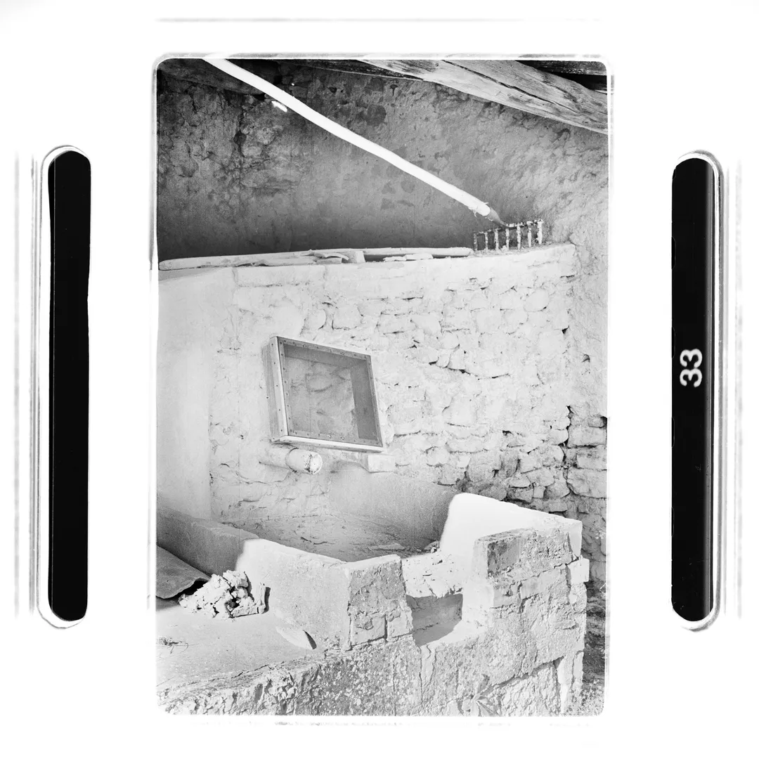 Photographie noir et blanc de l’intérieur d’un atelier de poterie à au poët-laval (Drôme) montrant un bassin maçonné et un mur en pierre, issue du reportage sur le potier Jacky Robin utilisant la terre blanche du village historique.