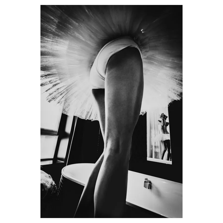 Contre-plongée sous le tutu du modèle ; reflet de Lala dans le miroir près de la baignoire, en tons de gris.