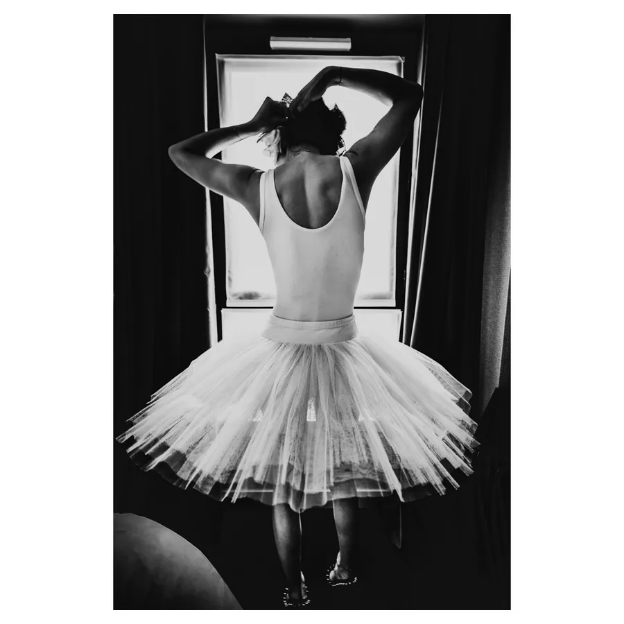 Le modèle féminin Lala, de dos devant la fenêtre, justaucorps et tutu en clair-obscur, se raccrochant les cheveux.