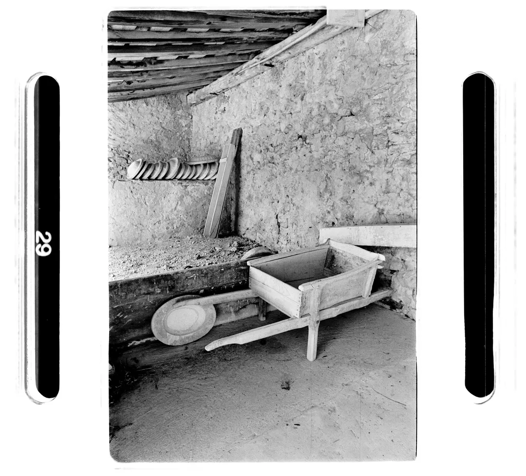 Photographie noir et blanc au poët-laval (Drôme) montrant l’intérieur d’un atelier de poterie avec une brouette en bois et un mur en pierre, issue du reportage sur le potier Jacky Robin travaillant la terre blanche locale.