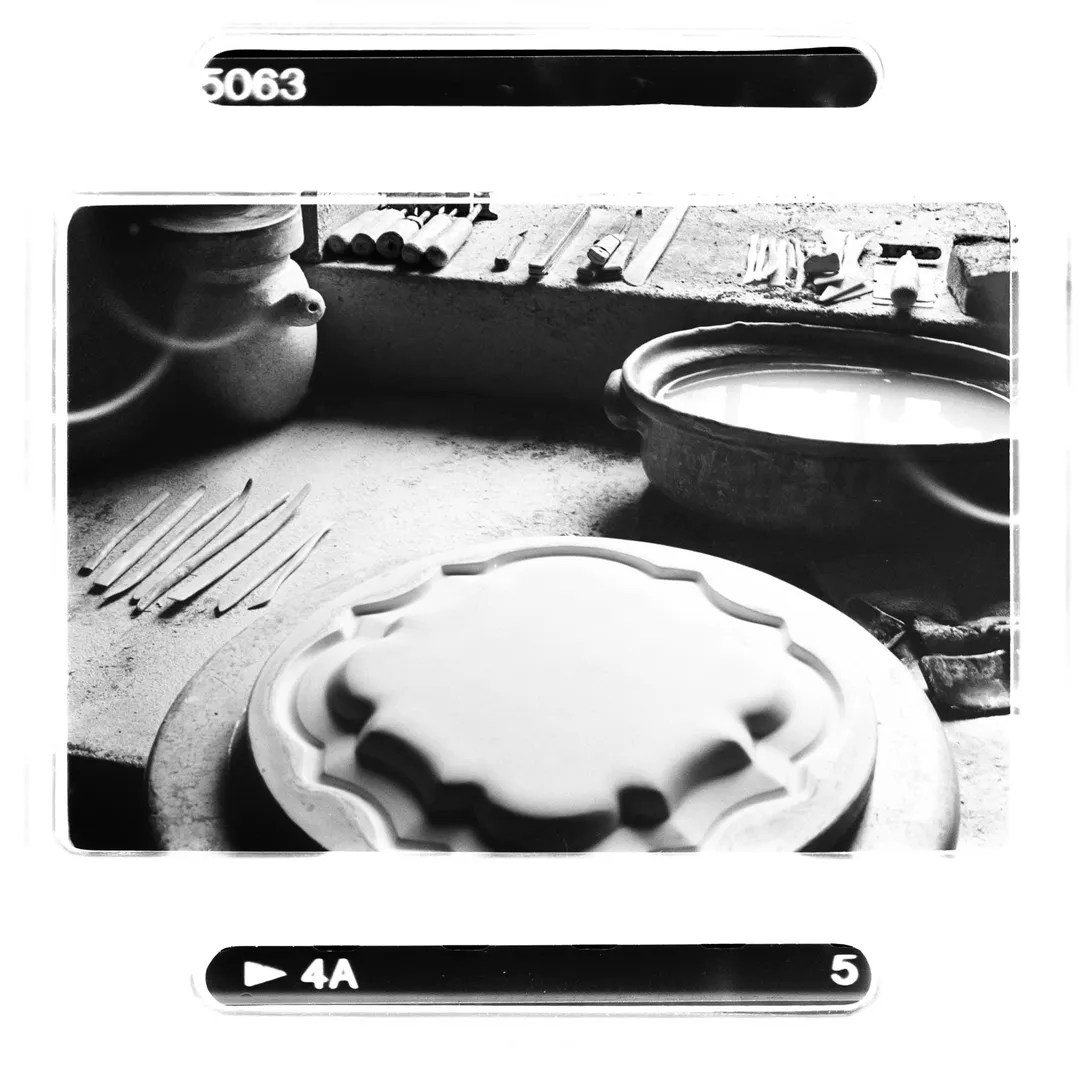 Photo noir et blanc d’un plan de travail de potier au poët-laval (Drôme) avec outils, moule de forme ronde et bassin de terre liquide, réalisée pour le reportage sur le potier Jacky Robin et la tradition de poterie en terre blanche du village.