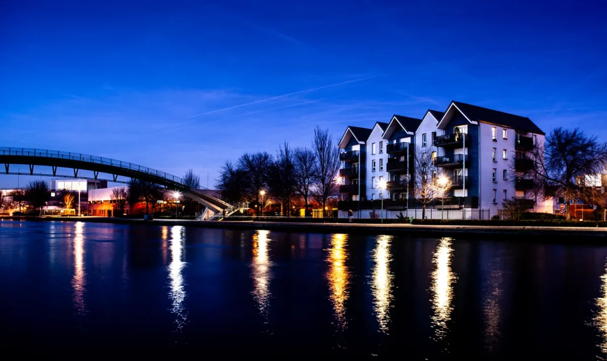 Photographie d’architecture en bord du canal Saint Denis au crépuscule avec immeubles contemporains, passerelle et reflets lumineux sur l’eau, réalisée par un photographe professionnel à Paris.