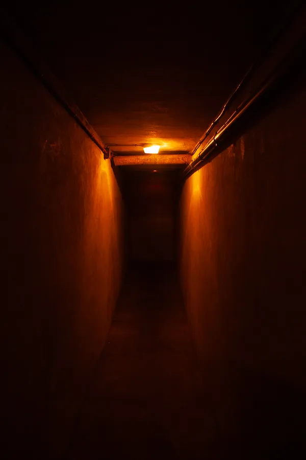 Photographie d’un couloir souterrain sombre avec éclairage orangé menant à une porte, réalisée par un photographe professionnel à Bayonne.
