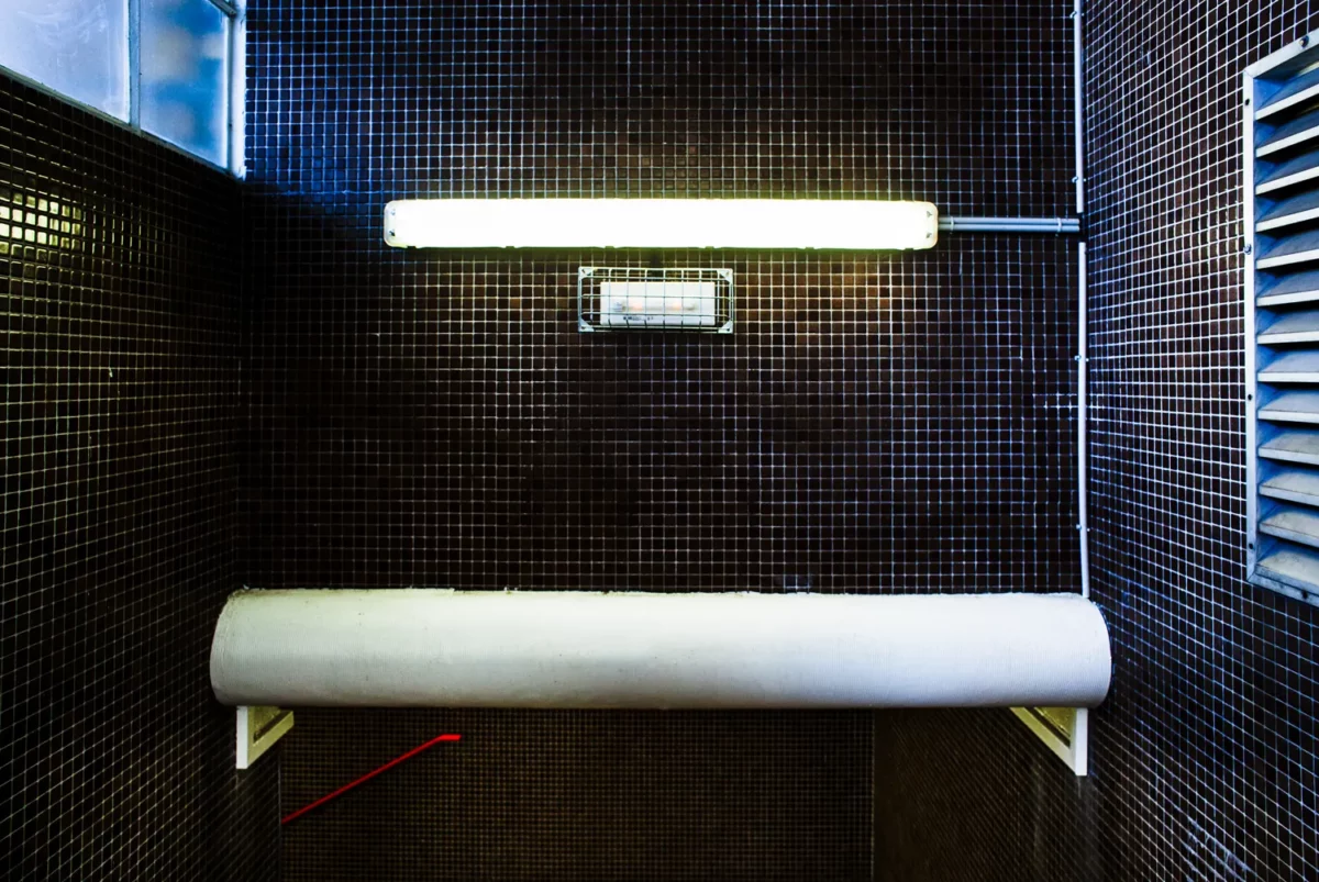 Photographie d’architecture intérieure d’un escalier au carrelage sombre avec luminaire fluorescent et détail industriel, réalisée par un photographe professionnel à Montélimar.