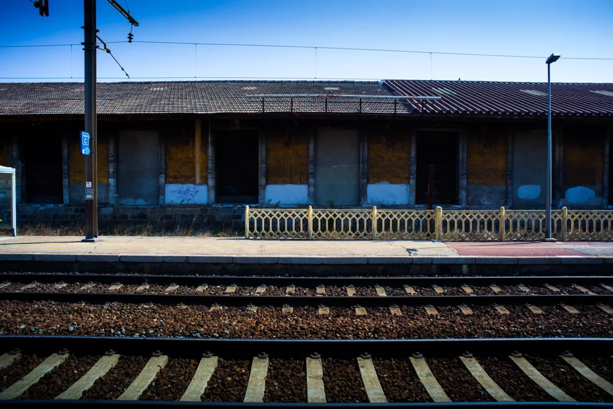 Photographie d’architecture d’un quai de gare au style industriel avec entrepôt en arrière-plan et voies ferrées au premier plan, réalisée par un photographe professionnel à Montélimar.