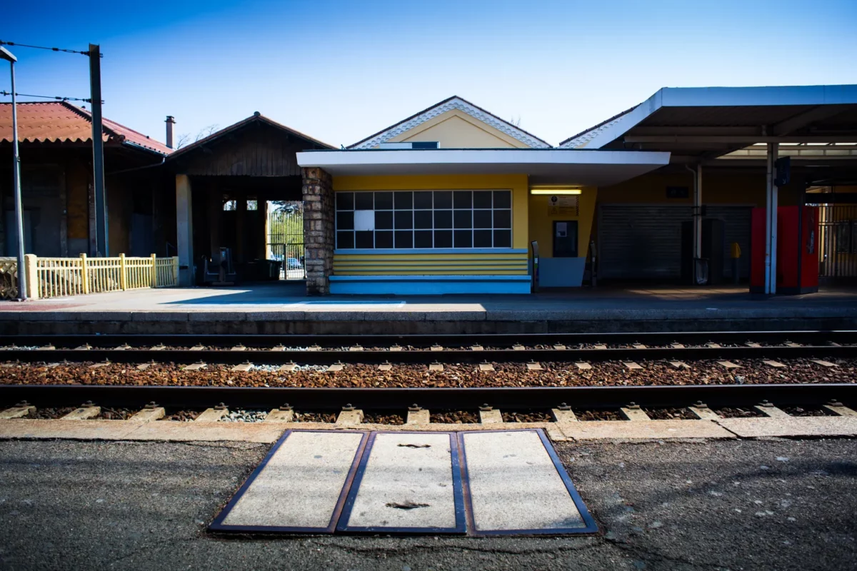 Photographie d’architecture d’un quai de gare avec bâtiment jaune et voies ferrées au premier plan, réalisée par un photographe professionnel à Montélimar.