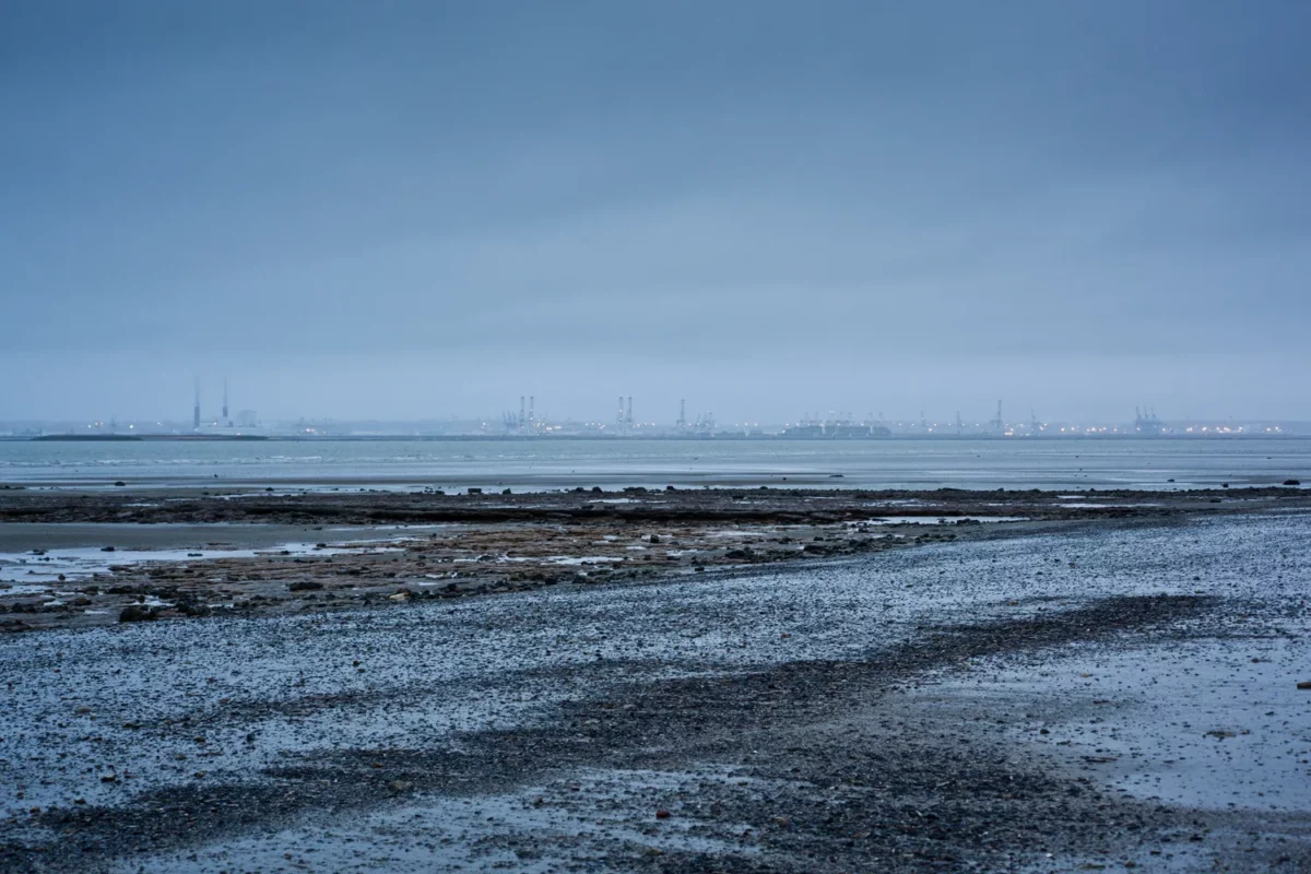 Photographie de paysage côtier à marée basse avec vue lointaine sur le port industriel du Havre éclairé, réalisée par un photographe professionnel