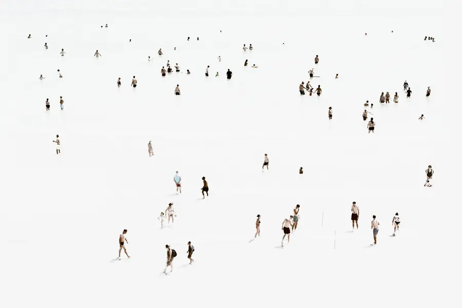 Photographie high-key en plan large aux sables-d'olonnes : nombreuses silhouettes de baigneurs dispersées sur une plage blanche à marée basse, lecture graphique des distances et des groupes, esthétique minimaliste et aérienne.