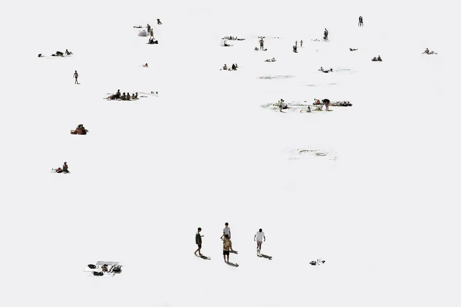 Photographie high-key en plan large aux sables d'olonne: petits groupes de baigneurs répartis sur un sable très clair, objets de plage minimalisés, longues ombres découpées, composition épurée qui accentue le vide et la distance entre les personnes.