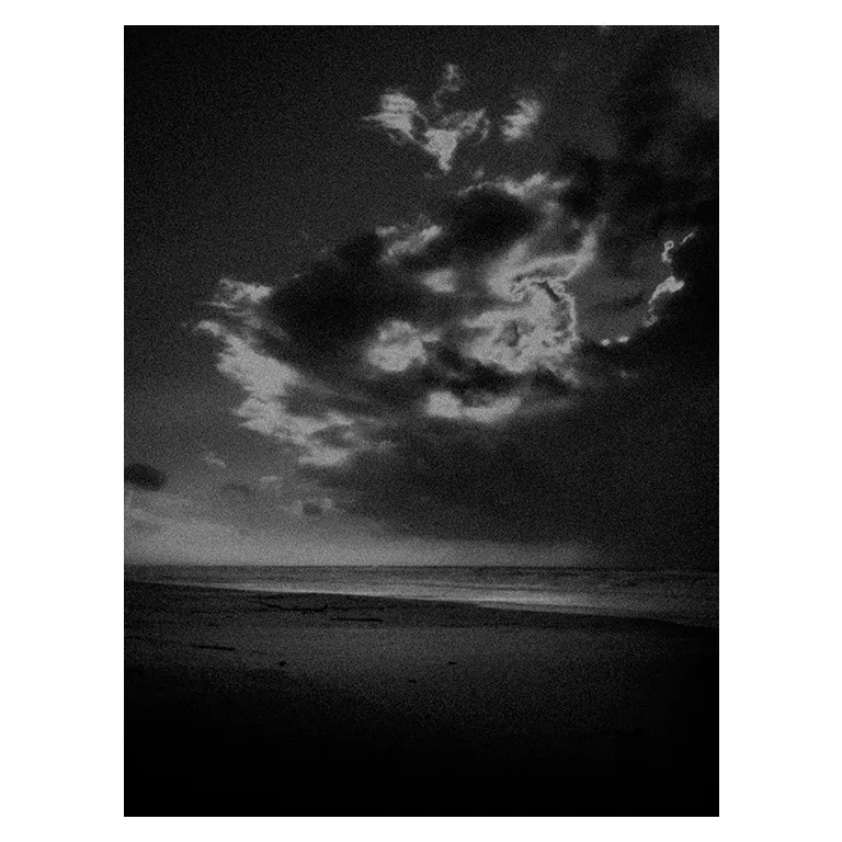 Photographie en noir et blanc très contrastée d’une plage atlantique au crépuscule, vaste ciel sombre avec amas de nuages éclairés par l’arrière, ligne de mer basse et sable obscur au premier plan, série « Marée intérieure » de Nicolas Louis.