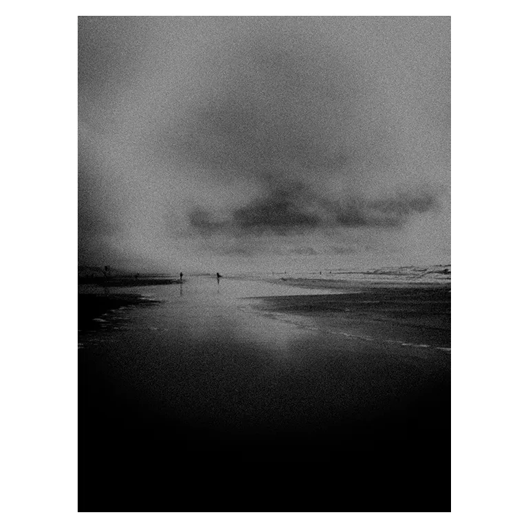 Photographie en noir et blanc très contrastée d’une plage atlantique : grande étendue d’eau en reflétant le ciel, horizon lointain, quelques silhouettes espacées et nuage sombre menaçant, série « Marée intérieure » de Nicolas Louis.