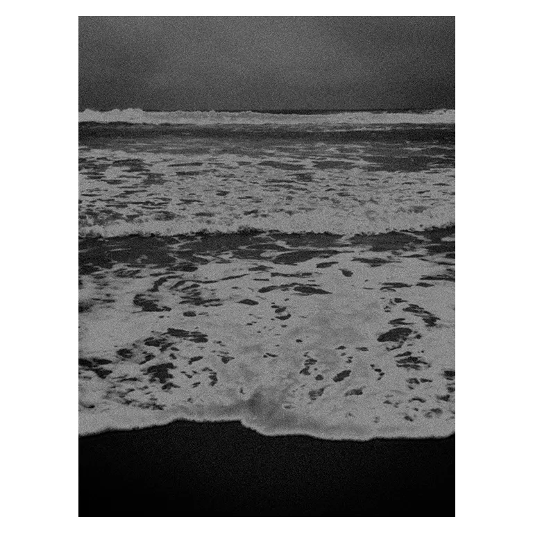 Photographie noir et blanc d'écumes : vagues superposées, ciel orageux, reflets sur le sable avec un rendu très contrasté au Porge ; un partie pris d’un rendu pictural plasticien.