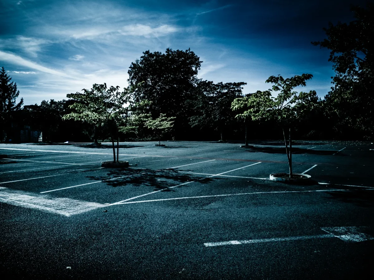 Photographie de paysage urbain d’un grand parking vide bordé d’arbres sous ciel bleu, réalisée par un photographe professionnel.