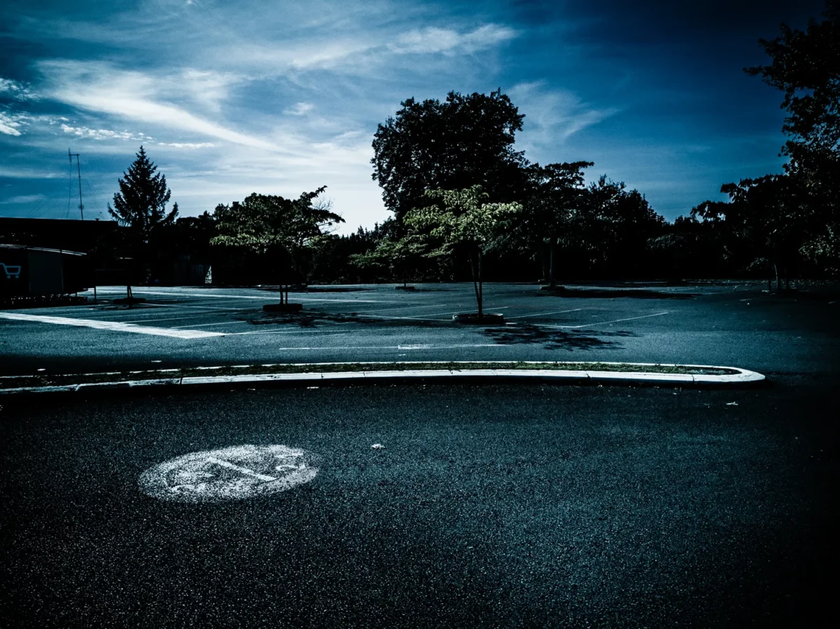 Photographie de paysage urbain d’un parking vide avec marquages au sol et petits arbres, réalisée par un photographe plasticien.