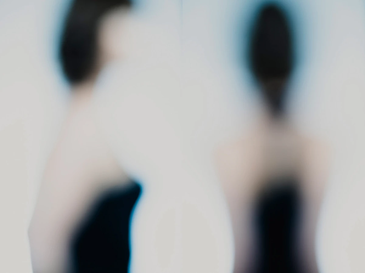 Photographie plasticienne défocalisée en diptyque : deux silhouettes vues de dos, robes sombres, contours dissous et halo lumineux central, palette douce — série photo « Erasure ».
