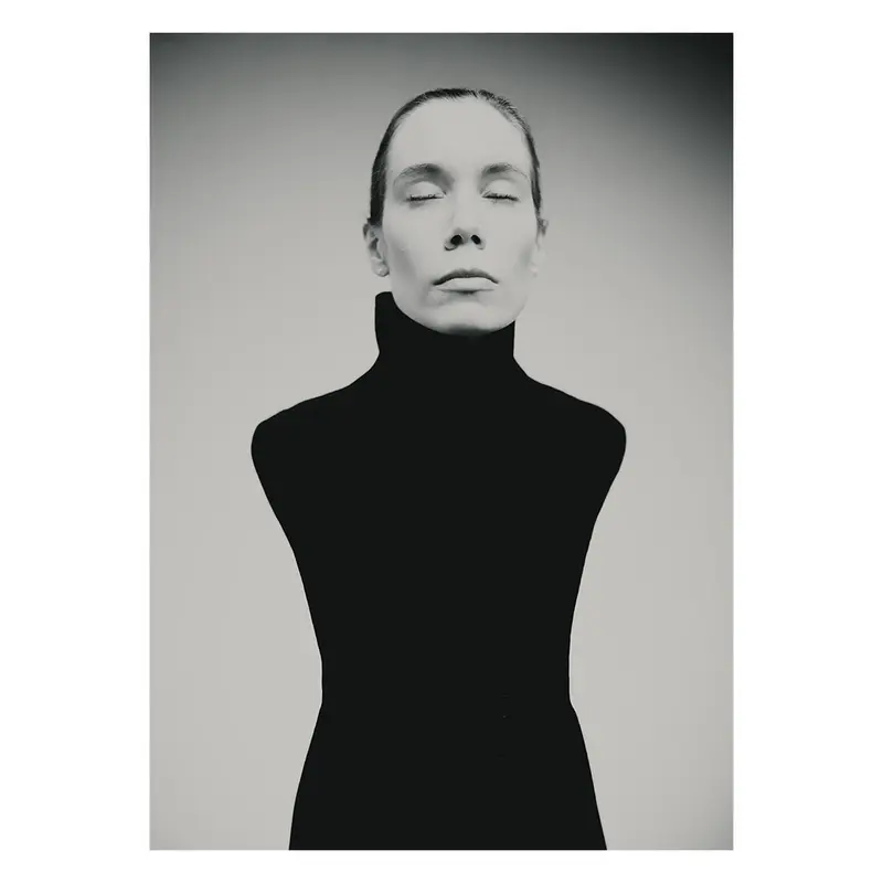 Portrait de femme en vêtement noir à col montant, composition minimaliste centrée sur le visage et la posture, photographie plasticienne en studio.