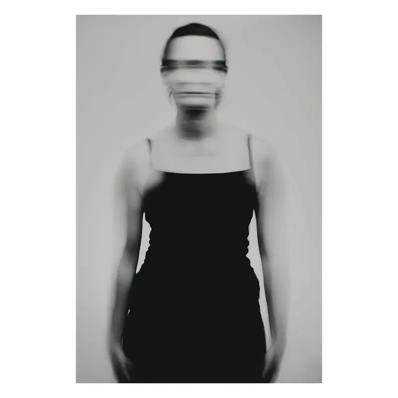 Photographie de portrait en studio, femme en robe noire sobre, pose frontale statique, recherche plasticienne sur la verticalité et l'élégance minimale.