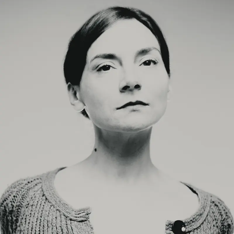 Portrait plasticien explorant la verticalité du regard d'une femme et la sobriété du vêtement avec le cou dégagé, pour une photographie en studio noir et blanc, composition épurée, modèle au centre.