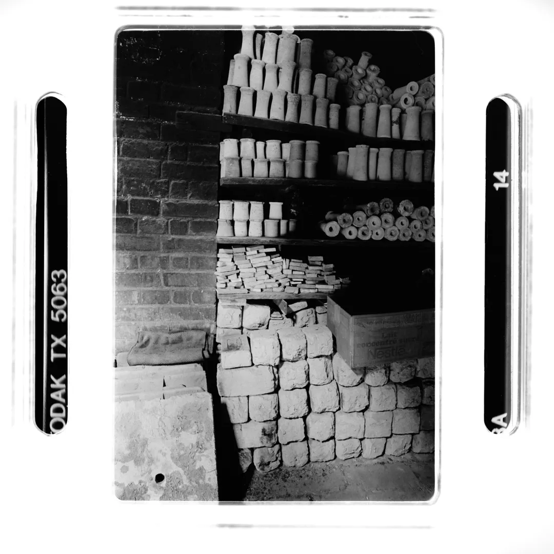 Photographie noir et blanc du stock de poterie au poët-laval (Drôme) avec briques de terre blanche et étagères remplies de pièces en cours de séchage, réalisée pour un reportage sur la poterie traditionnelle du village.