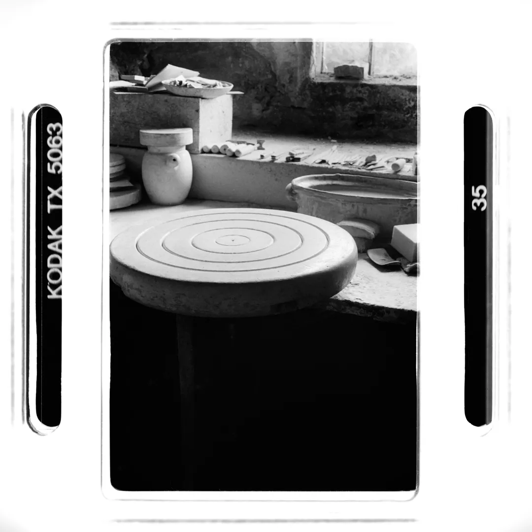 Photographie noir et blanc d’un tour de potier sur un plan de travail au poët-laval (Drôme), avec outils et bols près d’une fenêtre, prise dans le cadre d’un reportage sur la poterie traditionnelle du village.