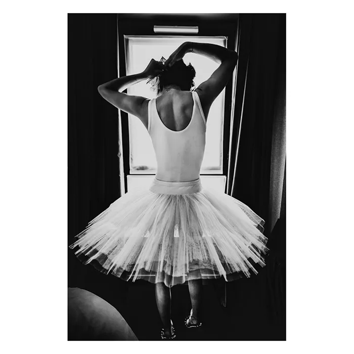 Le modèle féminin Lala, de dos devant la fenêtre, just au corps et tutu en clair-obscur, se raccrochant les cheveux. Série de portrait intime " Afternoon with Lala", par le photographe Nicolas Louis.