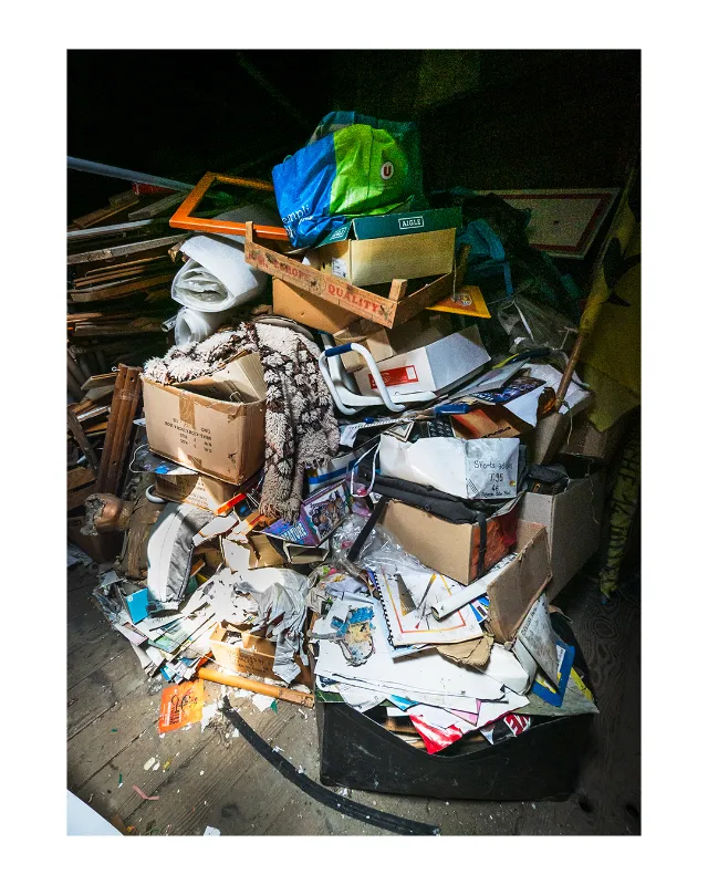 Composition photographique d'un amoncellement d'objets abandonnés : cartons, sacs, textiles et déchets entassés dans une benne, éclairés par un flash photographique créant des contrastes marqués sur fond noir, Dieulefit Drôme