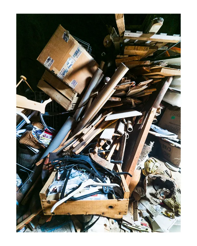 Vue plongeante sur un amoncellement désorganisé de planches de bois, cartons d'emballage, pinces à linge et objets divers empilés dans la pénombre d'un local de brocante à Dieulefit, Drôme, photographié avec lumière naturelle douce
