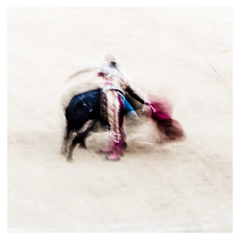 Photographie artistique de corrida à Bayonne : taureau noir et torero en cape rose fusionnent dans un flou de mouvement pictural, tons beiges et pourpres, hommage au style Ernst Haas, effet impressionniste