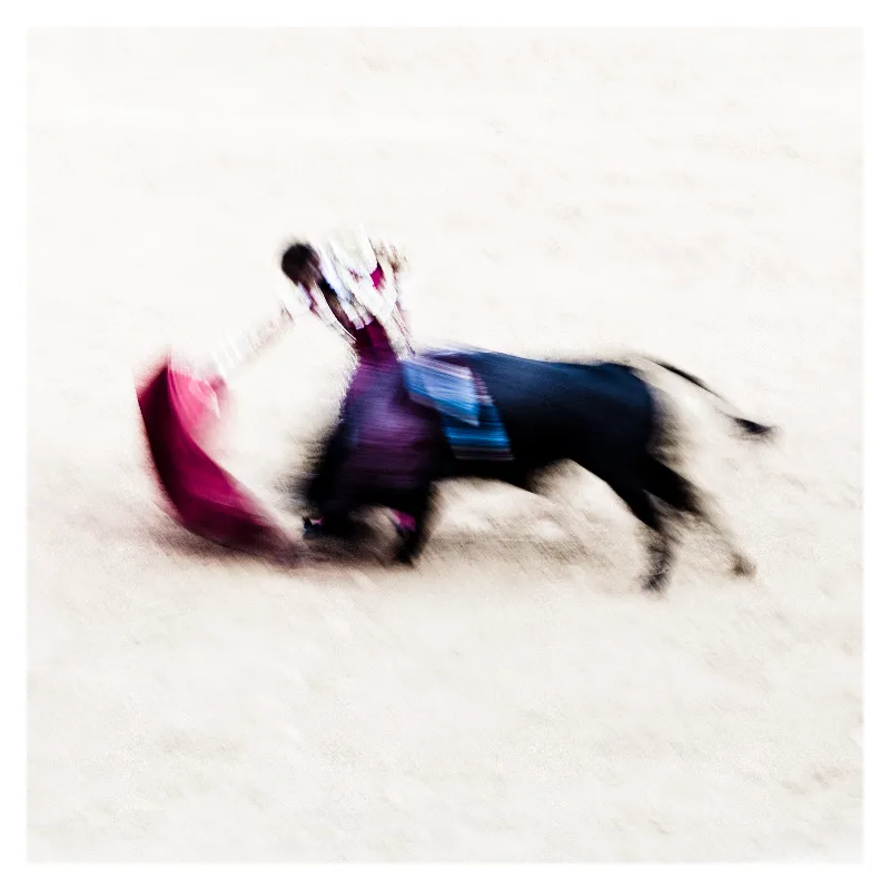 Photographie artistique d'un taureau chargeant une cape rose magenta en mouvement, effet de flou cinétique créant une abstraction picturale aux tons violets et bleus, inspirée du style Ernst Haas