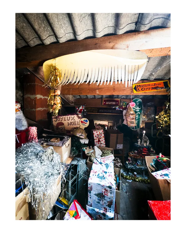Intérieur chaleureux d'une brocante artisanale à Dieulefit dans la Drôme, avec décorations de Noël suspendues, enseigne en bois Joyeux Noël, guirlandes argentées et objets vintage sous lumière naturelle douce