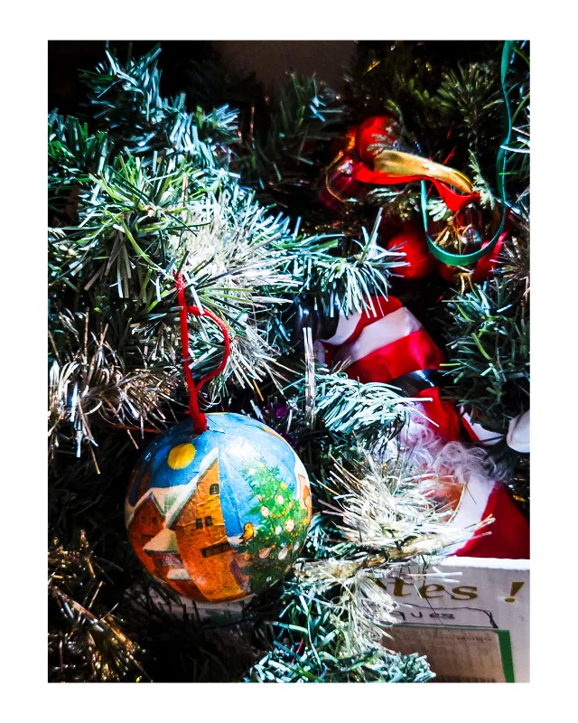 Composition festive de décorations de Noël vintage : boule artisanale peinte à la main représentant un paysage de village avec église et sapin, entourée de guirlandes argentées scintillantes et figurines du Père Noël sur branches de sapin naturel