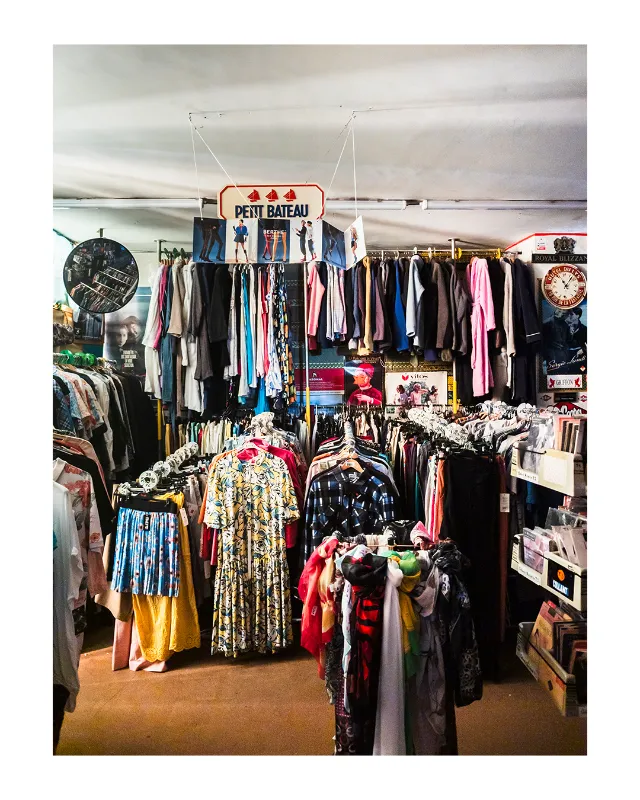 Photographie d'intérieur d'une boutique Petit Bateau à Dieulefit dans la Drôme, montrant des portants chargés de vêtements colorés, des horloges murales vintages et une ambiance chaleureuse de commerce de proximité