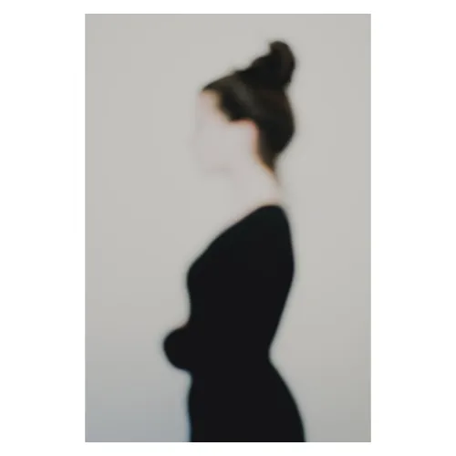 Photographie artistique plasticienne défocalisée : silhouette féminine de profil, chignon et tenue sombre, contours adoucis et identité estompée, fond neutre minimaliste — extrait de la série de portrait « Erasure », par le photographe Nicolas Louis