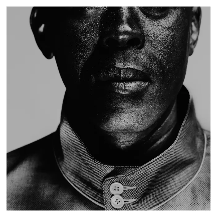 Gros plan artistique en noir et blanc sur le bas du visage d'un homme, mettant en relief le grain de la peau et une barbe naissante, portant une veste à col officier boutonné, photographie de studio réalisée à Bagnolet par Nicolas Louis.