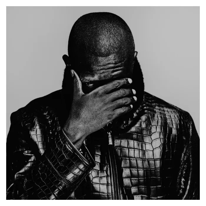 Portrait d'art masculin en noir et blanc, homme posant la main devant le visage avec un seul œil visible, portant un blouson en cuir à texture crocodile, éclairage de studio dramatique réalisé à Bagnolet par Nicolas Louis.