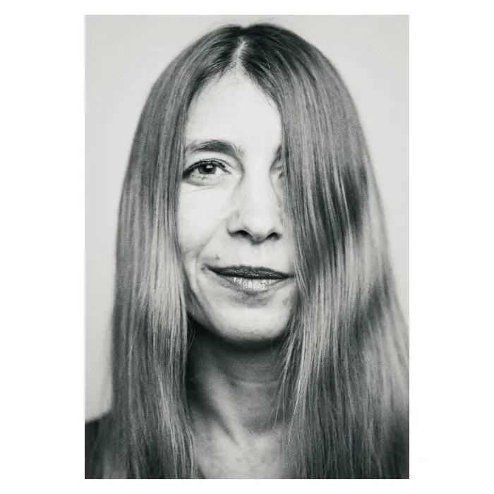 Portrait frontal en noir et blanc d'une femme au sourire discret, longs cheveux lisses dont une mèche voile légèrement le côté gauche du visage, regard clair et serein, photographie de studio épurée réalisée au Vésinet par Nicolas Louis."