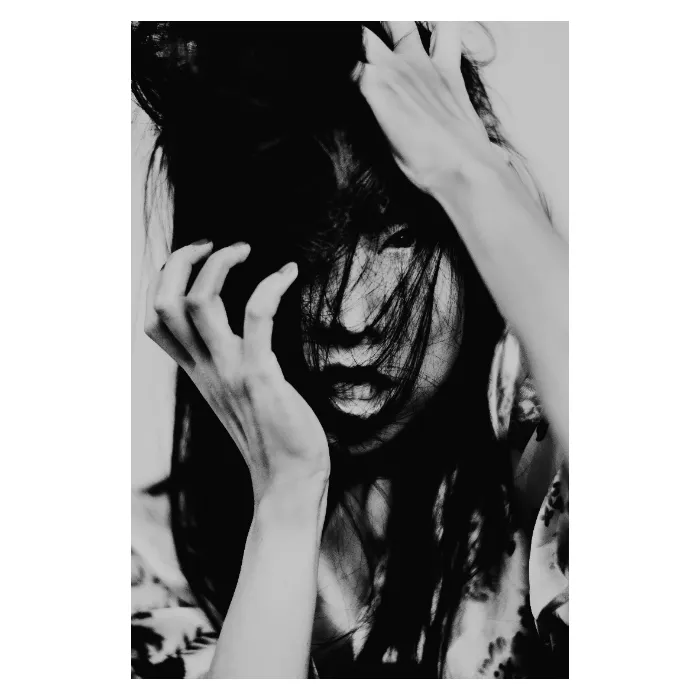 Portrait artistique en noir et blanc d'une femme aux mains dans les cheveux, visage partiellement masqué par des mèches sombres, expression intense et dramatique, photographie de studio contrastée réalisée au Vésinet par Nicolas Louis.