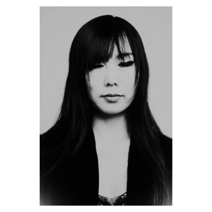 Portrait frontal en noir et blanc d'une jeune fille aux yeux clos, visage paisible et serein, cheveux attachés en chignon haut avec quelques mèches libres, portant un polo blanc au col bordé d'un liseré sombre, photographie de studio épurée réalisée au Vésinet par Nicolas Louis.