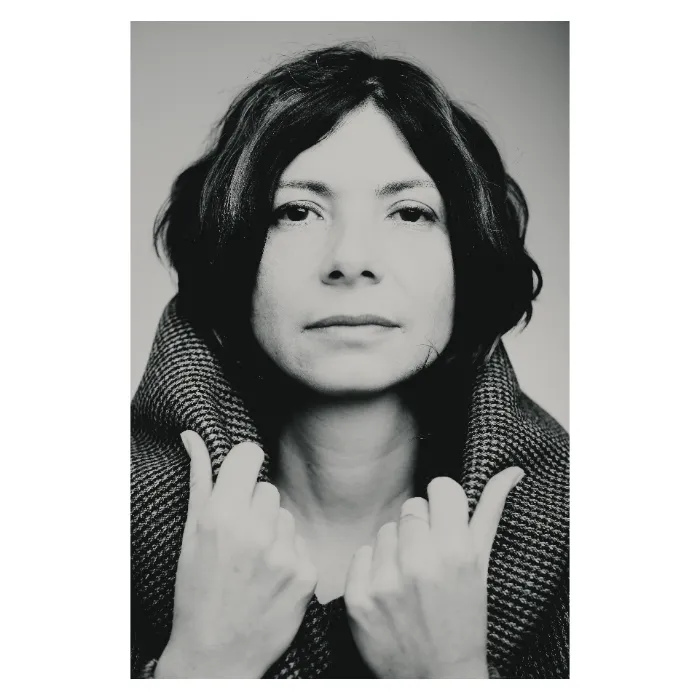 Portrait de face en noir et blanc d'une femme au regard serein, les mains relevant le col d'un manteau en maille épaisse texturée, photographie de studio épurée réalisée à Bagnolet par Nicolas Louis.